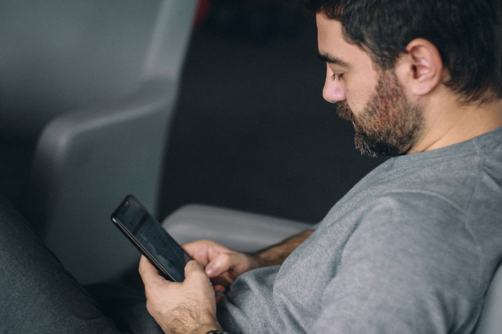 A man in a grey shirt looks down at his cellphone